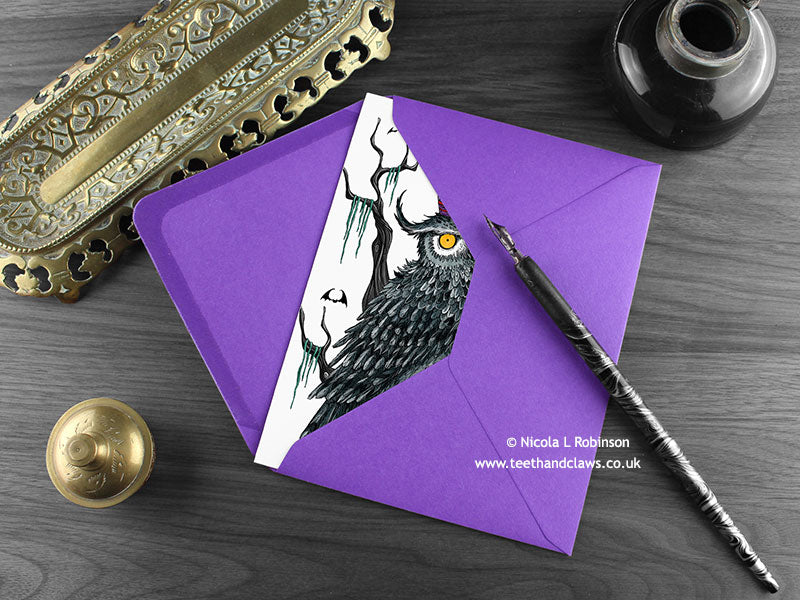 Gothic Owl birthday card, shown lying flat, with my original pen and ink illustration of a birthday owl, inside an open purple envelope. With vintage Victorian pen and writing desk accessories. Design and illustration © Nicola L Robinson | Teeth and Claws