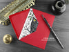 Gothic Owl Christmas card, shown lying flat, with my original pen and ink illustration of an owl, inside an open red envelope. With vintage Victorian pen and writing desk accessories. Design and illustration © Nicola L Robinson | Teeth and Claws