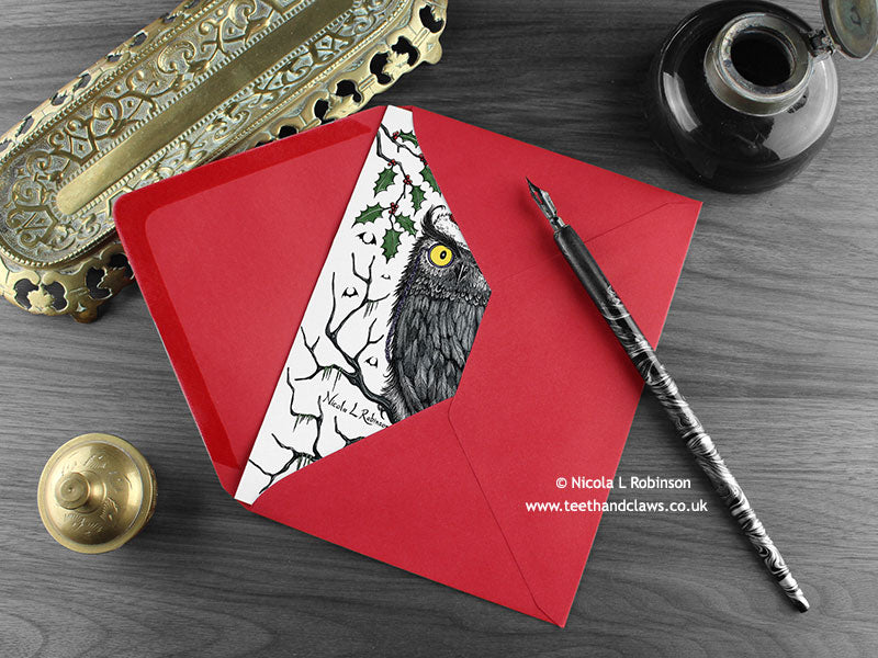 Gothic Owl Christmas card, shown lying flat, with my original pen and ink illustration of an owl, inside an open red envelope. With vintage Victorian pen and writing desk accessories. Design and illustration © Nicola L Robinson | Teeth and Claws