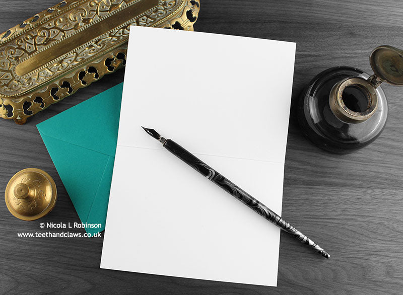 Persian cat greeting card, shown open and flat with blank inside, on a teal envelope, alongside vintage Victorian pen and writing desk accessories. Design and illustration © Nicola L Robinson | Teeth and Claws