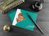 Persian cat greeting card, shown lying flat, with my original pen and ink illustration of a Persian cat, inside an open teal envelope. With vintage Victorian pen and writing desk accessories. Design and illustration © Nicola L Robinson | Teeth and Claws
