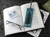 Raven bookmark featuring my original pen and ink illustration, back view of the bookmark resting on an open book with reading glasses and one of my branded cards. Made in the UK. Design and illustration © Nicola L Robinson | Teeth and Claws.