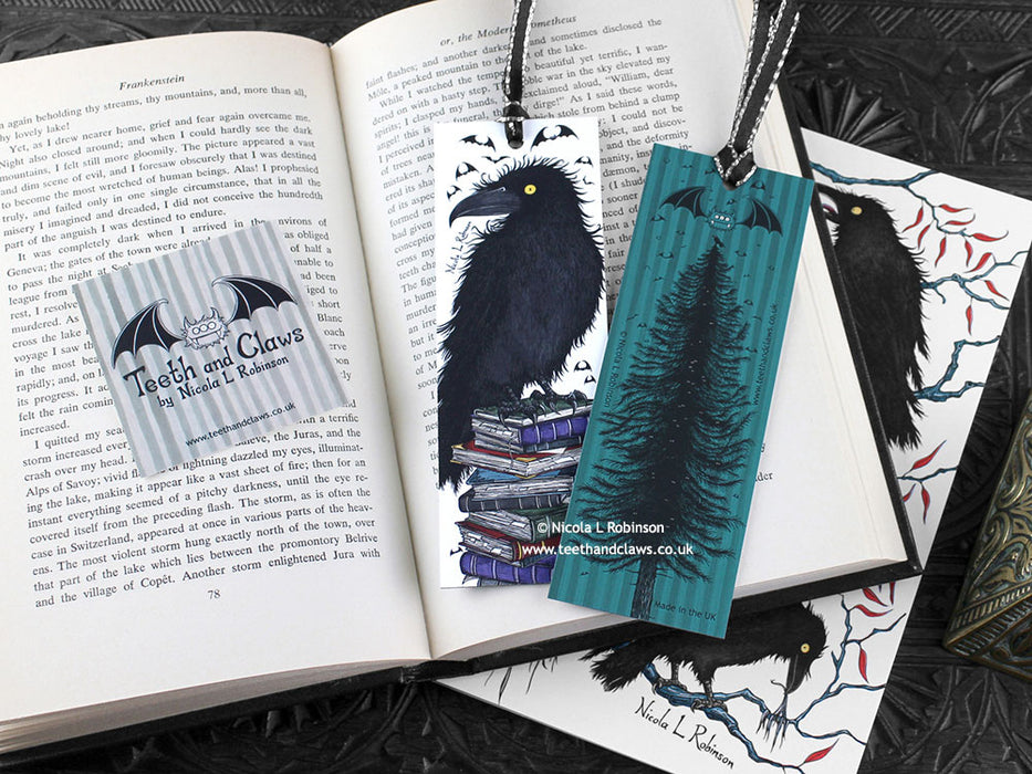 Raven bookmark featuring my original pen and ink illustrations, front and back view of the bookmark resting on an open book with one of my branded cards. Made in the UK. Design and illustration © Nicola L Robinson | Teeth and Claws.