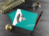 Ragdoll cat greeting card, shown lying flat, with my original pen and ink illustration of a ragdoll cat, inside an open teal envelope. With vintage Victorian pen and writing desk accessories. Design and illustration © Nicola L Robinson | Teeth and Claws