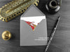 Red Dragon greeting card, shown lying flat, with my original pen and ink illustration of a red dragon, inside an open grey envelope. With vintage Victorian pen and writing desk accessories. Design and illustration © Nicola L Robinson | Teeth and Claws