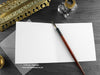 Roaring red dragon greeting card, shown open and flat with blank inside, on a grey envelope, alongside vintage Victorian pen and writing desk accessories. Design and illustration © Nicola L Robinson | Teeth and Claws