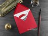 Persian Cat Christmas card, shown lying flat, with my original pen and ink illustration of a festive cat, inside an open red envelope. With vintage Victorian pen and writing desk accessories. Design and illustration © Nicola L Robinson | Teeth and Claws