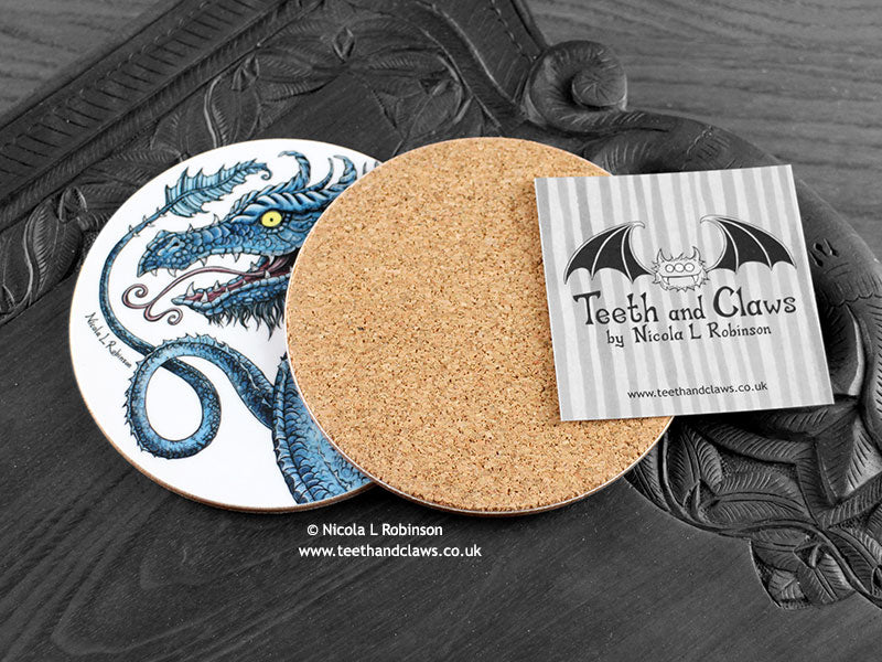 Blue Dragon Coaster featuring my original pen and ink illustration of a blue dragon, back view showing the cork backing, alongside one of my branded cards. Made in the UK. Design and illustration © Nicola L Robinson | Teeth and Claws.
