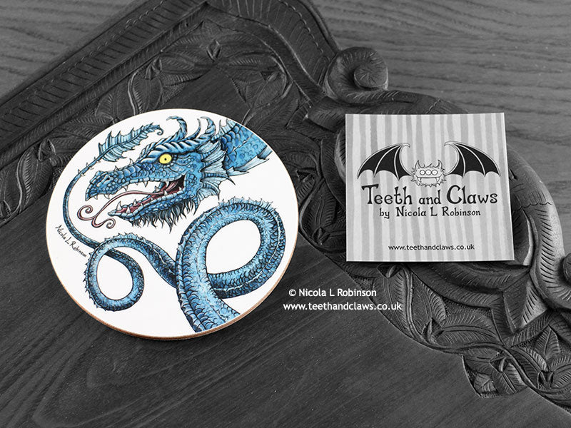 Blue Dragon Coaster featuring my original pen and ink illustration of a blue dragon, front view alongside one of my branded cards. Made in the UK. Design and illustration © Nicola L Robinson | Teeth and Claws.