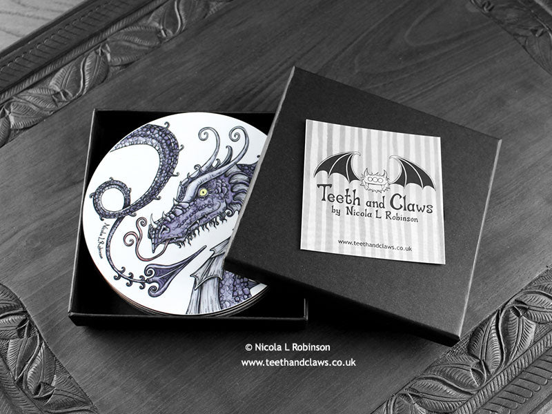 Set of four of my dragon coasters featuring my original pen and ink dragon illustrations, front view in an open black gift box with card. Made in the UK. Design and illustration © Nicola L Robinson | Teeth and Claws.