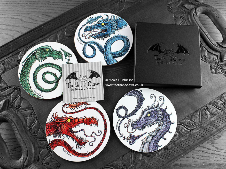 Set of four of my dragon coasters featuring my original pen and ink dragon illustrations, front view alongside a black gift box and card. Made in the UK. Design and illustration © Nicola L Robinson | Teeth and Claws.