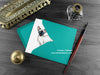 Siamese cat greeting card, shown lying flat, with my original pen and ink illustration of a cat, inside an open teal envelope. With vintage Victorian pen and writing desk accessories. Design and illustration © Nicola L Robinson | Teeth and Claws
