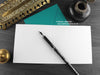Sorry Cat Greeting card, shown open and flat with blank inside, on a teal envelope, alongside vintage Victorian pen and writing desk accessories. Design and illustration © Nicola L Robinson | Teeth and Claws