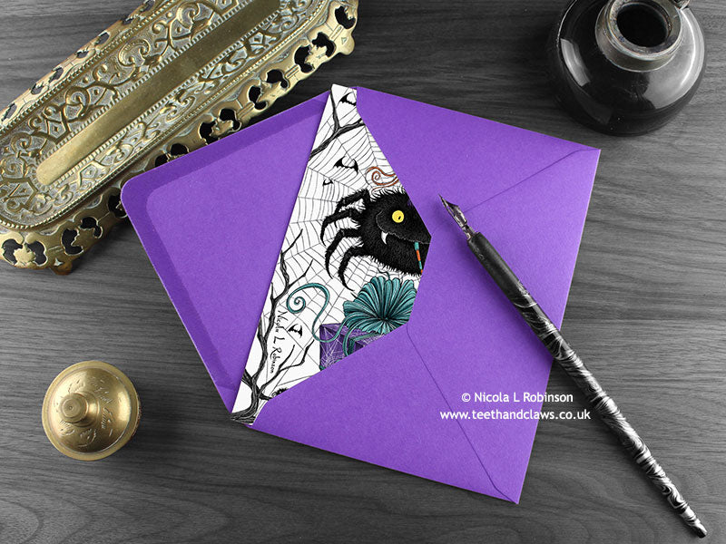 Spider birthday card, shown lying flat, with my original pen and ink spider illustration, inside an open purple envelope. With vintage Victorian pen and writing desk accessories. Design and illustration © Nicola L Robinson | Teeth and Claws