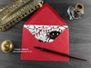 Spider love card, shown lying flat, with my original pen and ink illustration of two spiders, inside an open red envelope. With vintage Victorian pen and writing desk accessories. Design and illustration © Nicola L Robinson | Teeth and Claws