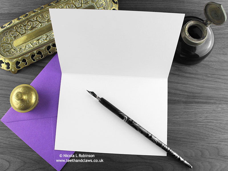 Spider birthday card, shown open and flat with blank inside, on a purple envelope, alongside vintage Victorian pen and writing desk accessories. Design and illustration © Nicola L Robinson | Teeth and Claws