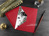 Spider Christmas card, shown lying flat, with my original pen and ink illustration of a festive spider, inside an open red envelope. With vintage Victorian pen and writing desk accessories. Design and illustration © Nicola L Robinson | Teeth and Claws