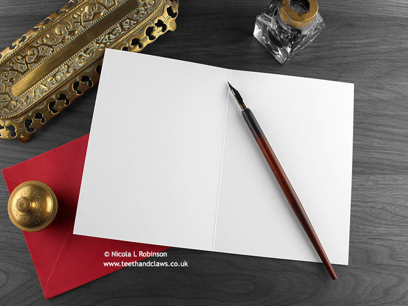Spiders Christmas card, shown open and flat with blank inside, on a red envelope, alongside vintage Victorian pen and writing desk accessories. Design and illustration © Nicola L Robinson | Teeth and Claws