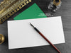 Dinosaur Birthday card, shown open and flat with blank inside, on a green envelope, alongside vintage Victorian pen and writing desk accessories. Design and illustration © Nicola L Robinson | Teeth and Claws