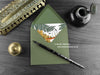 Stegosaurus and ferns greeting card, shown lying flat, with my original pen and ink illustration of a dinosaur, inside an open green envelope. With vintage Victorian pen and writing desk accessories. Design and illustration © Nicola L Robinson | Teeth and Claws.