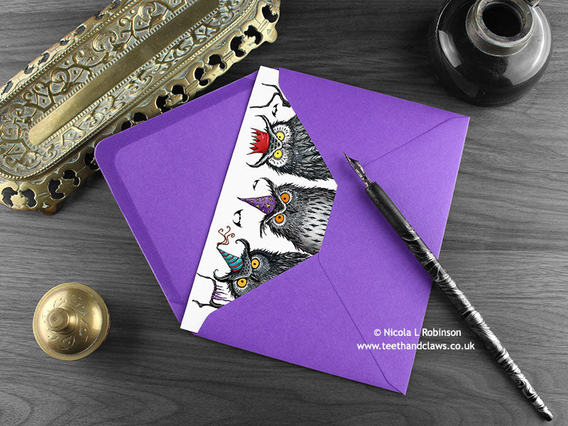 Owls birthday card, shown lying flat, with my original pen and ink illustration of owls, inside an open purple envelope. With vintage Victorian pen and writing desk accessories. Design and illustration © Nicola L Robinson | Teeth and Claws