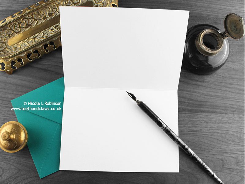Tom cat and kitten greeting card, shown open and flat with blank inside, on a teal envelope, alongside vintage Victorian pen and writing desk accessories. Design and illustration © Nicola L Robinson | Teeth and Claws