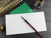 Dinosaur greeting card, shown open and flat with blank inside, on a green envelope, alongside vintage Victorian pen and writing desk accessories. Design and illustration © Nicola L Robinson | Teeth and Claws