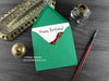 Dinosaur Birthday card, shown lying flat, with my original pen and ink illustration of a T rex, inside an open green envelope. With vintage Victorian pen and writing desk accessories. Design and illustration © Nicola L Robinson | Teeth and Claws