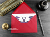 Dinosaur love card, shown lying flat, with my original pen and ink illustration of two dinosaurs, inside an open red envelope. With vintage Victorian pen and writing desk accessories. Design and illustration © Nicola L Robinson | Teeth and Claws
