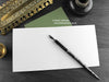 Triceratops and ferns greeting card, shown open and flat with blank inside, on a green envelope, alongside vintage Victorian pen and writing desk accessories. Design and illustration © Nicola L Robinson | Teeth and Claws