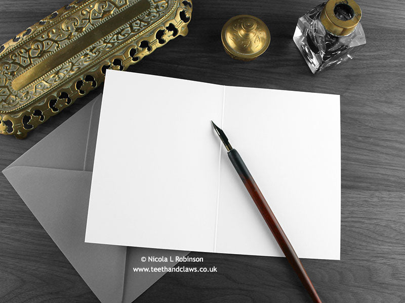 Purple Dragons New Baby Twins Card, shown open and flat with blank inside, on a grey envelope, alongside vintage Victorian pen and writing desk accessories. Design and illustration © Nicola L Robinson | Teeth and Claws