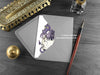 Purple Dragons New Baby Twins Card,, shown lying flat, with my original pen and ink illustration of two dragons, inside an open grey envelope. With vintage Victorian pen and writing desk accessories. Design and illustration © Nicola L Robinson | Teeth and Claws