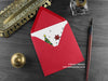 Dinosaur Christmas card, shown lying flat, with my original pen and ink illustration of a festive ankylosaurus, inside an open red envelope. With vintage Victorian pen and writing desk accessories. Design and illustration © Nicola L Robinson | Teeth and Claws