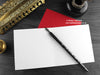Dragon Christmas card, shown open and flat with blank inside, on a red envelope, alongside vintage Victorian pen and writing desk accessories. Design and illustration © Nicola L Robinson | Teeth and Claws
