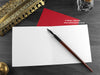 Triceratops Christmas card, shown open and flat with blank inside, on a red envelope, alongside vintage Victorian pen and writing desk accessories. Design and illustration © Nicola L Robinson | Teeth and Claws