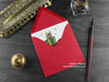 Dinosaur Christmas card, shown lying flat, with my original pen and ink illustration of a festive triceratops, inside an open red envelope. With vintage Victorian pen and writing desk accessories. Design and illustration © Nicola L Robinson | Teeth and Claws
